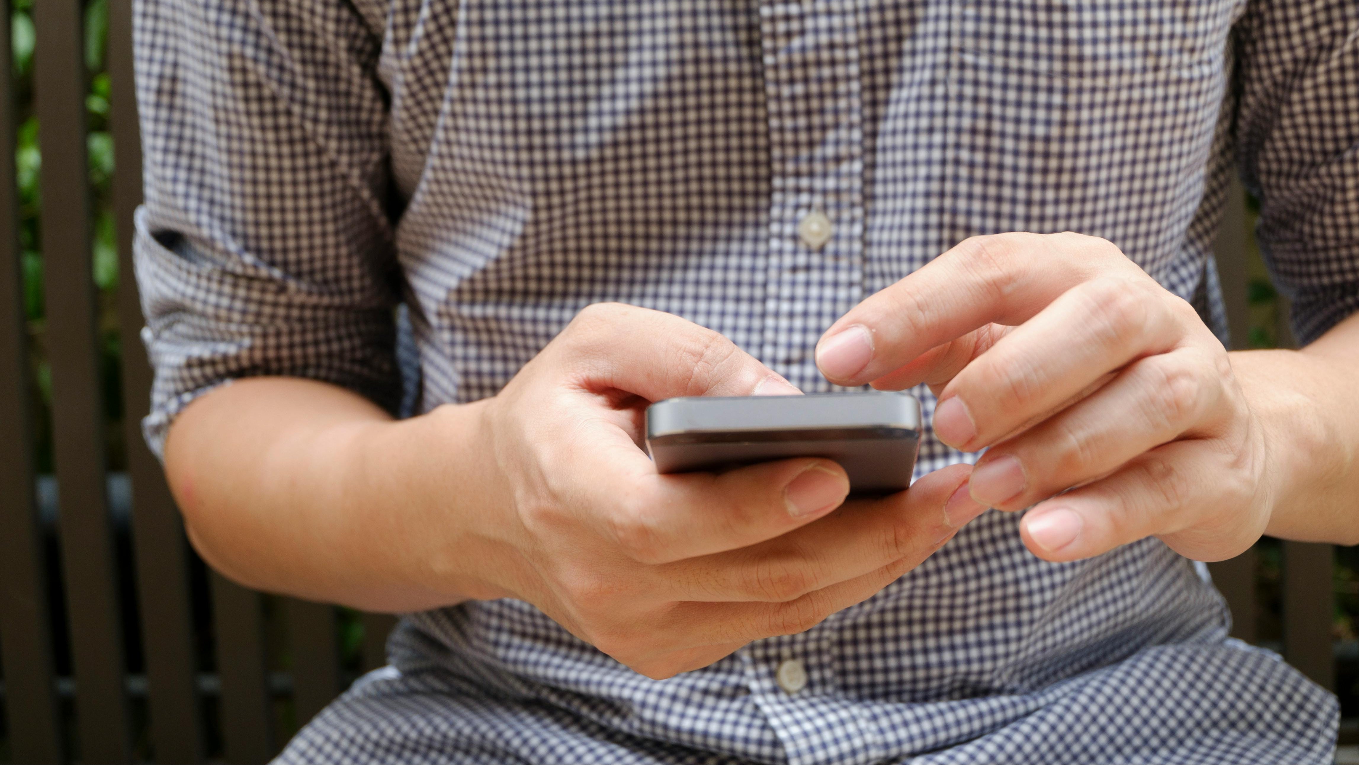 Person using a smartphone with a checkered shirt in an outdoor setting
